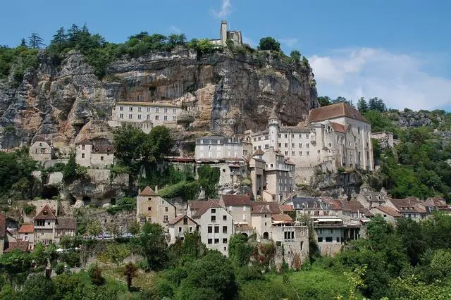 A historic town built into a steep cliffside, featuring stone buildings, a castle, and a church under a clear blue sky.