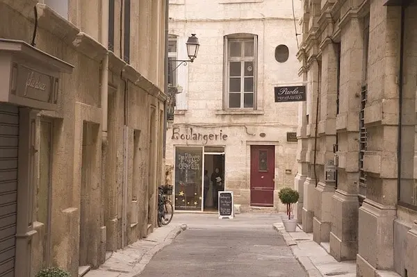 Narrow European street with a boulangerie shop, a bicycle, and a red door.