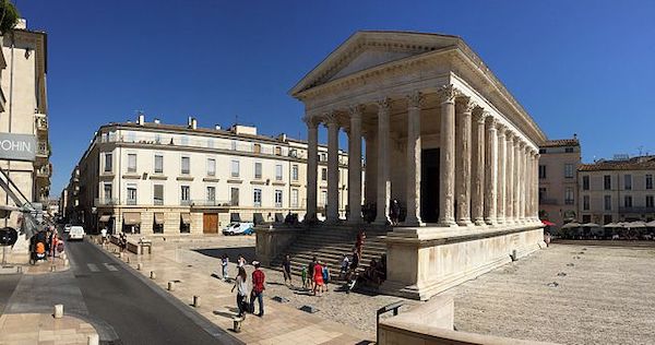 Maison Carrée, a Roman temple with Corinthian columns, stands in a sunny plaza with people gathered on its steps and in the surrounding square.