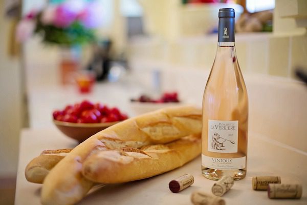 Bottle of Domaine de la Verriere Ventoux rosé wine with two baguettes and a bowl of cherry tomatoes.