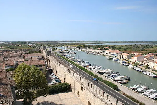 Aerial view of a walled town with a canal lined with boats and buildings.