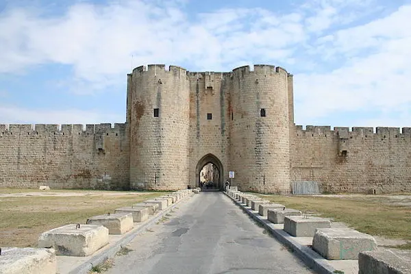 A stone fortress with two large round towers flanking an arched gateway. A road leads to the gate, lined with concrete blocks.