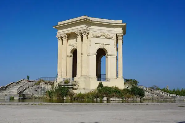 A Palladian-style building with columns and arches stands beside a body of water with a grand staircase leading up to it.