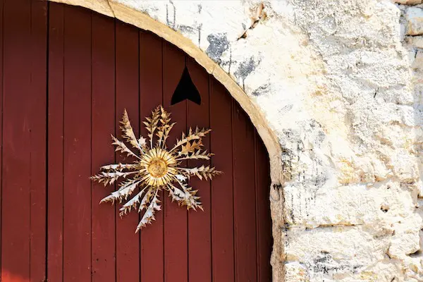 A decorative golden sunburst adorns a dark red wooden door, framed by a rough stone archway.