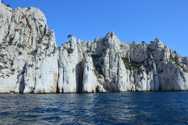 Towering white limestone cliffs with sparse green vegetation rise dramatically from the deep blue sea under a clear sky.