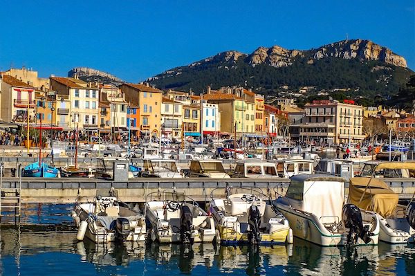 Colorful buildings line a harbor filled with boats, with a rocky, tree-covered mountain in the background.
