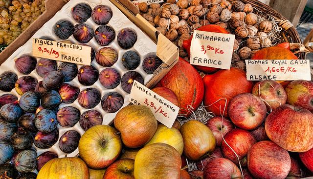 Fresh figs, pumpkins, apples, and walnuts for sale at a market. Signs indicate prices for figs and apples.