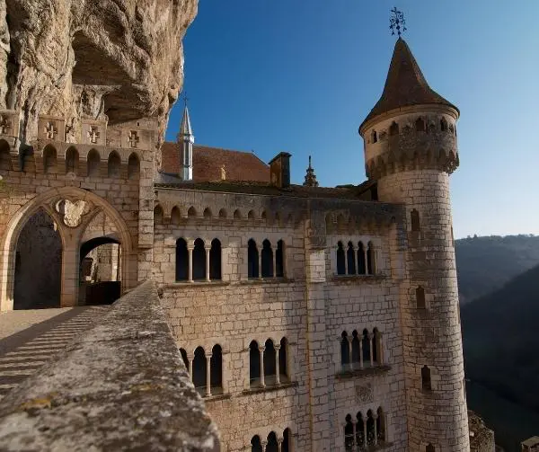 Stone castle built into a cliff face, with a tall tower and arched windows.