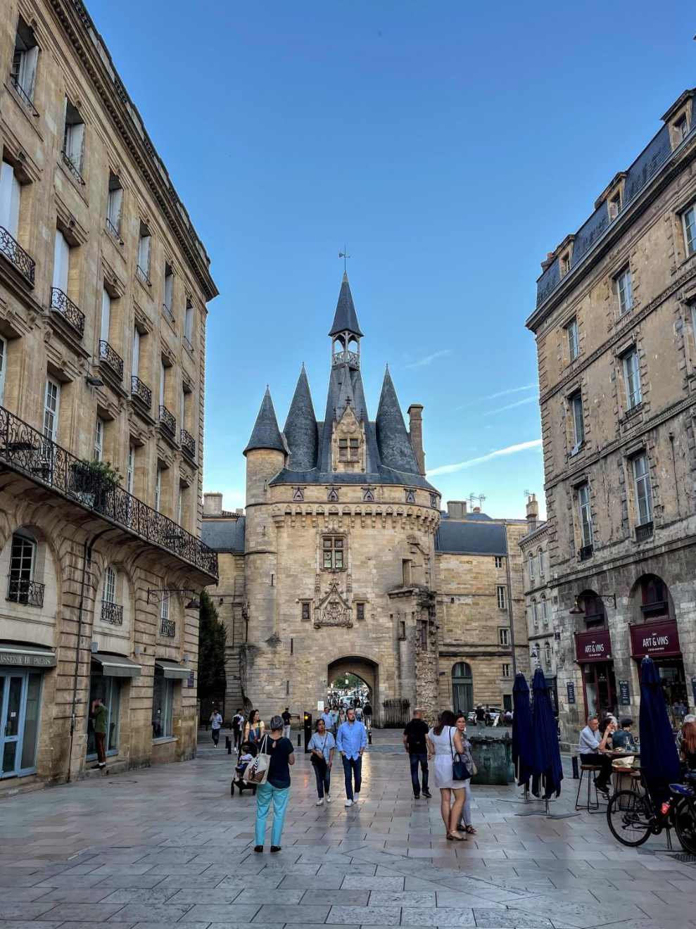 The Grosse Cloche gate in Bordeaux, France, with people walking in a plaza lined with stone buildings.