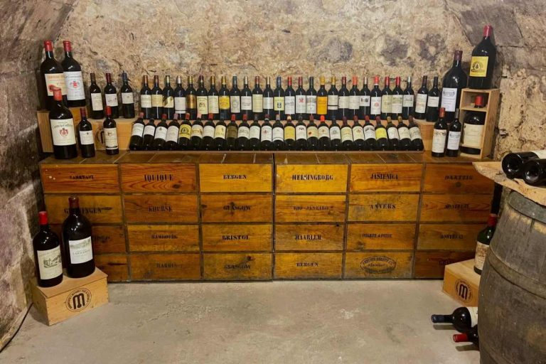 Rows of wine bottles displayed on wooden crates labeled with city names like Bergen, Helsingborg, and Antwerp.