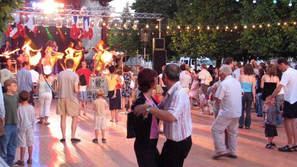 People dancing outside, musicians on stage, string lights overhead, one couple focused in center