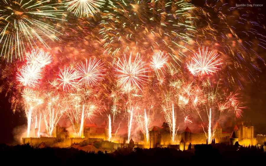 Red and white fireworks explode over a silhouetted castle at night, Bastille Day France.