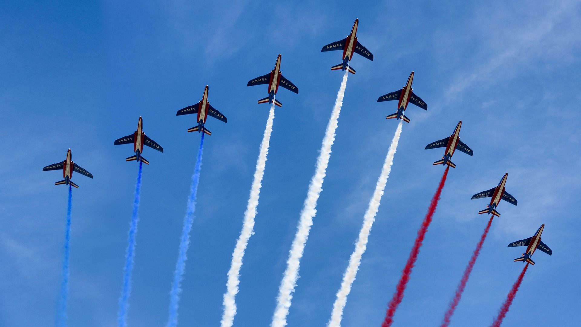 Planes overhead in formation with blue, red, and white smoke trails