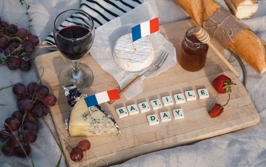 Picnic spread with cheese, grapes, baguette, wine, strawberries, and Bastille Day spelled out in tiles.