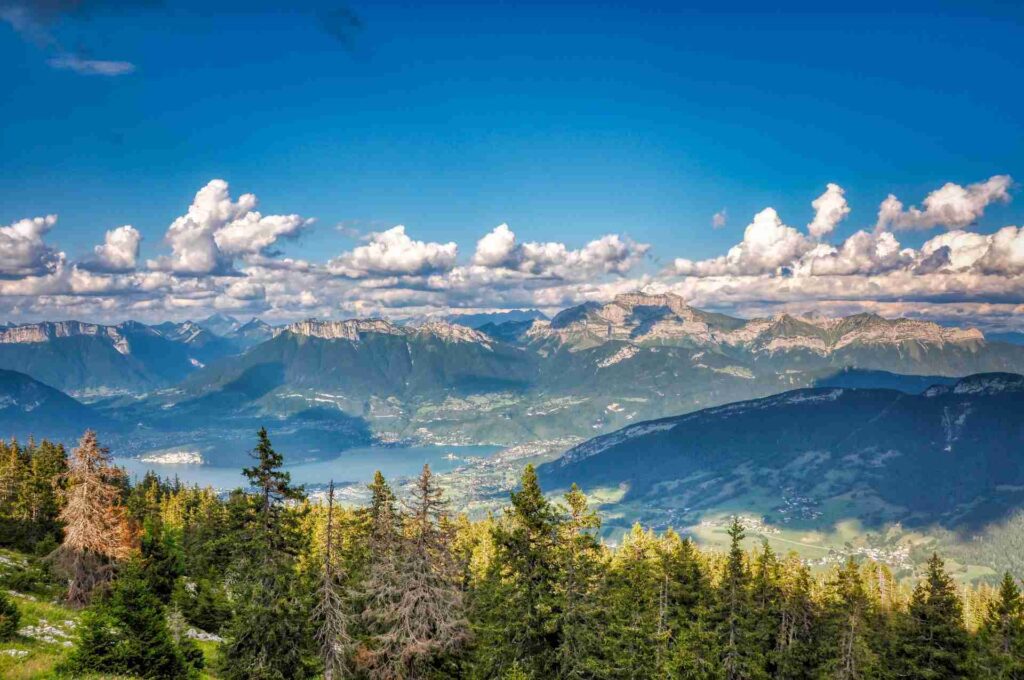 View from mountaintop over the lake and treetops, clouds and mountains in the distance