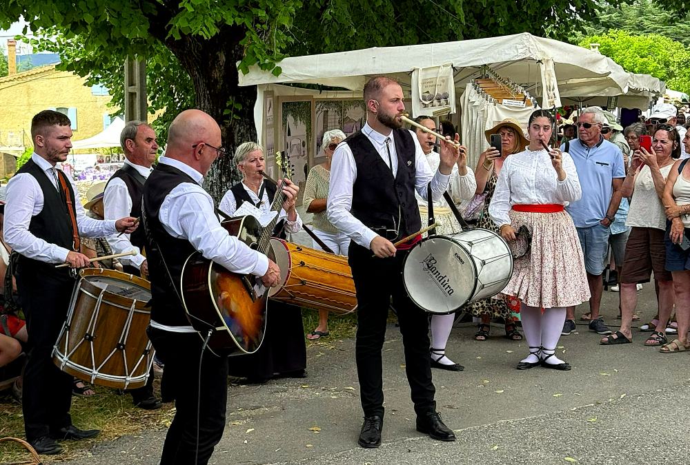 A traditional band plays music at an outdoor festival with people watching and taking photos