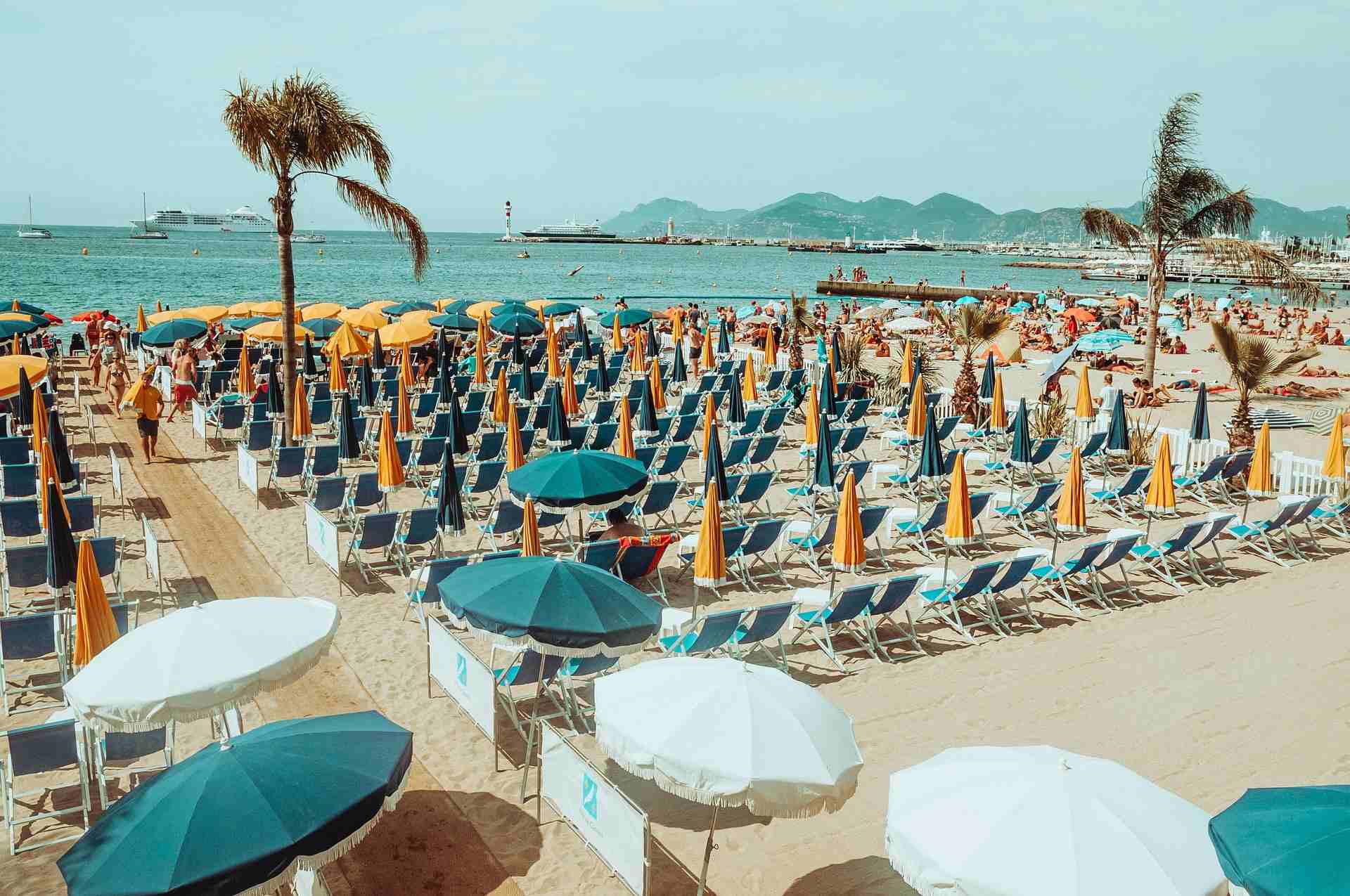 Blue and orange beach chairs and umbrellas in rows, boats and mountains in background