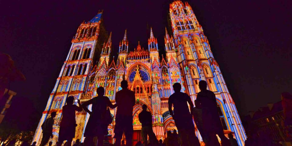 Cathedral facade colorfully illuminated by night with shadows of onlookers