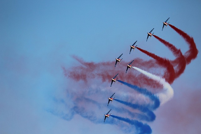A squadron of nine fighter jets flies in formation, trailing red, white, and blue smoke across a clear blue sky.
