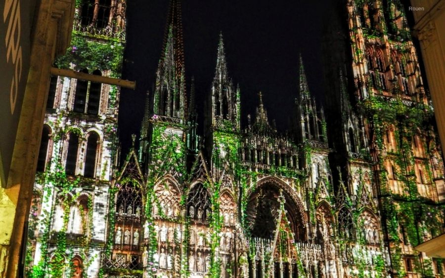 Rouen Cathedral illuminated at night with lush green ivy covering its gothic architecture.