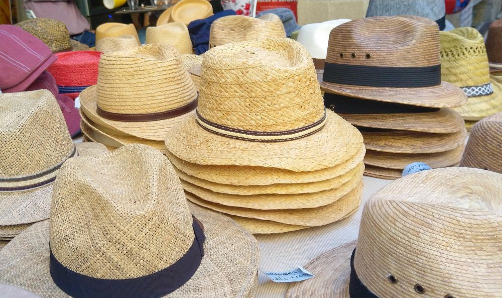 A variety of straw fedora hats are displayed at an outdoor market.