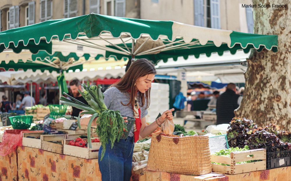 Woman shops for fresh produce at a vibrant outdoor market in the South of France.