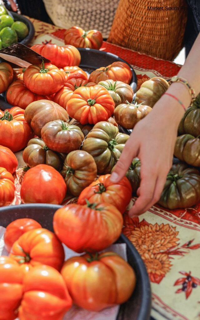 Assortment of colorful heirloom tomatoes at a market with a hand reaching to pick one.