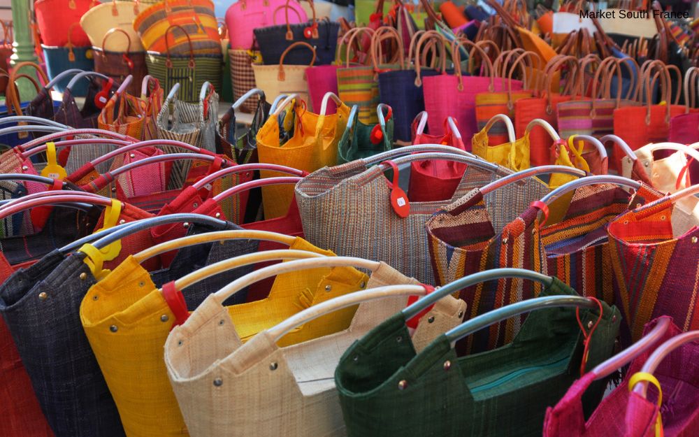 Colorful woven bags and tote bags are displayed at an outdoor market.