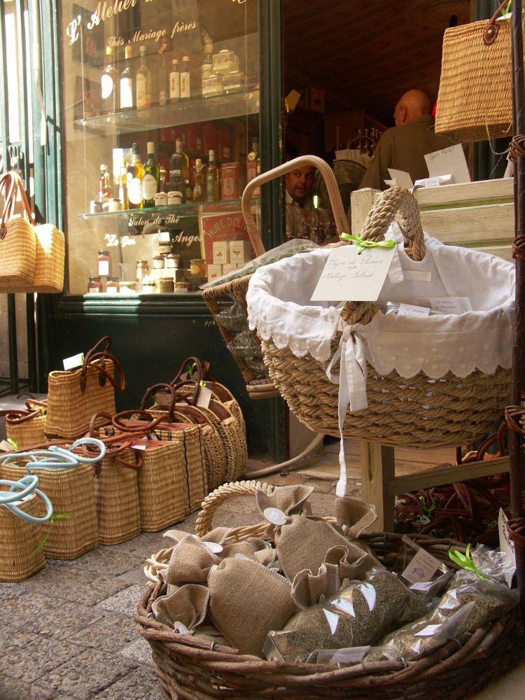 Wicker baskets overflowing with market goods in front of a shop window displaying bottles and jars.