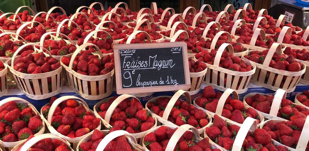 Baskets of fresh strawberries at a market with a sign indicating Magnum strawberries for 9 euros per kilogram.